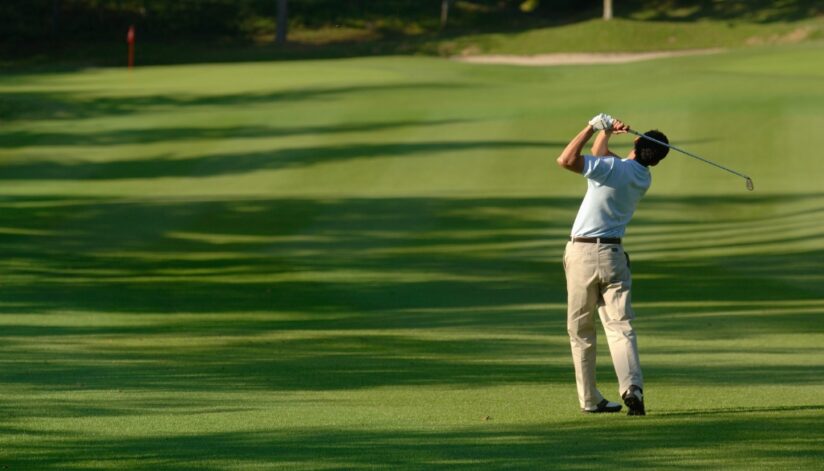 A golfer is taking his swing on the green.