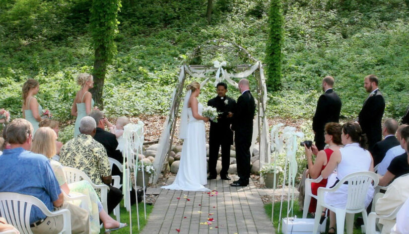 A bride and groom exchange vows at an outdoor altar at Drugan’s Castle Mound, surrounded by guests and tall trees in Holmen, WI.