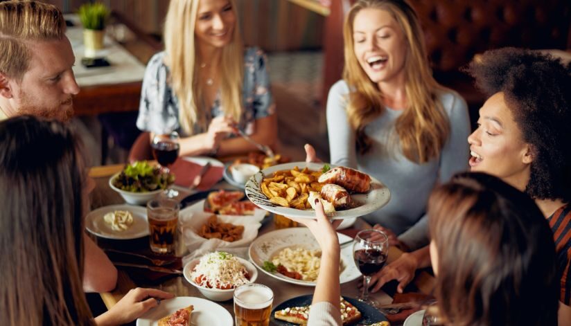A group of friends share plates of food and enjoy a meal together at a restaurant table.