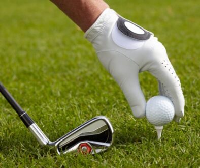 On the lush fairway at Drugan’s Castle Mound in Holmen, Wisconsin, a gloved hand sets a golf ball on a tee near a club.