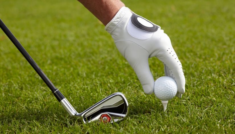 On the lush fairway at Drugan’s Castle Mound in Holmen, Wisconsin, a gloved hand sets a golf ball on a tee near a club.