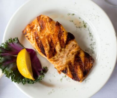 At Drugan’s Castle Mound in Holmen, Wisconsin, a grilled salmon fillet rests on a white plate with lemon, greens, and herbs.