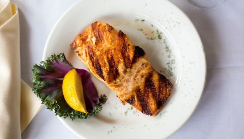 At Drugan’s Castle Mound in Holmen, Wisconsin, a grilled salmon fillet rests on a white plate with lemon, greens, and herbs.
