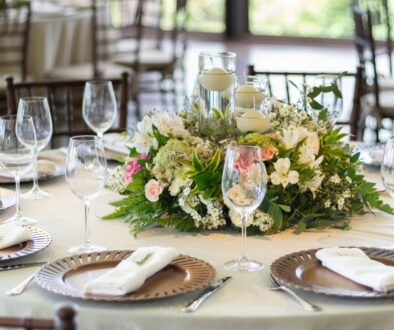 A round table formally set with glassware, folded napkins, and a floral centerpiece.