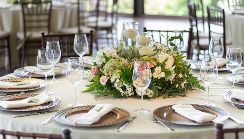 A round table formally set with glassware, folded napkins, and a floral centerpiece.