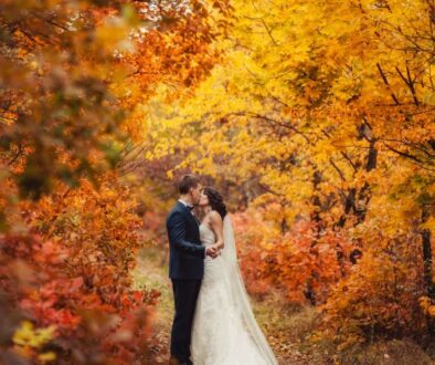 A bride and groom embrace and kiss on a path at Drugan’s Castle Mound, framed by vibrant red, orange, and yellow autumn trees.