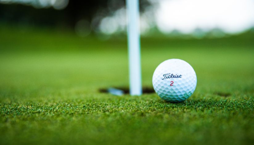 A Titleist golf ball sits close to the hole on the green at Drugan’s Castle Mound in Holmen, Wisconsin, with the flagstick behind.
