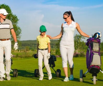 A family of three, each carrying a golf bag and dressed in sporty attire, walks across the green at Drugan’s Castle Mound in Holmen, WI.