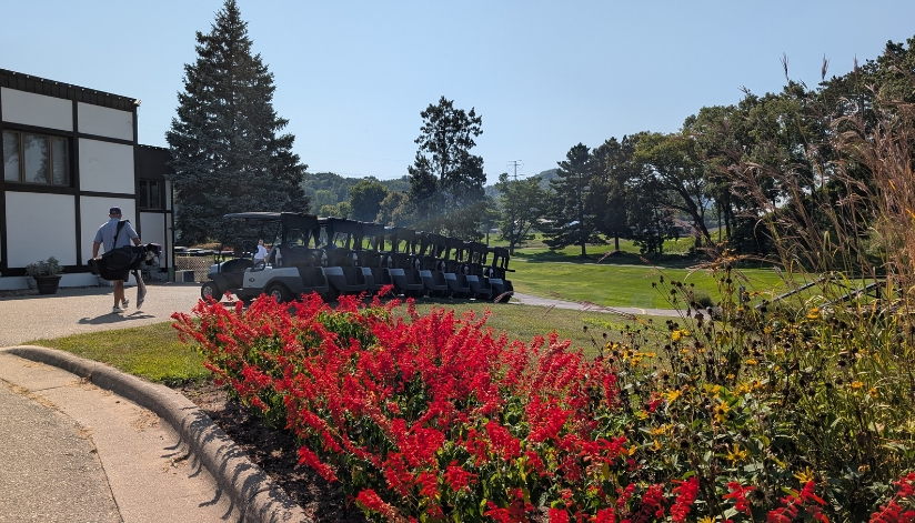At Drugan’s Castle Mound in Holmen, golf carts line up by red flowers as a golfer walks by carrying clubs.