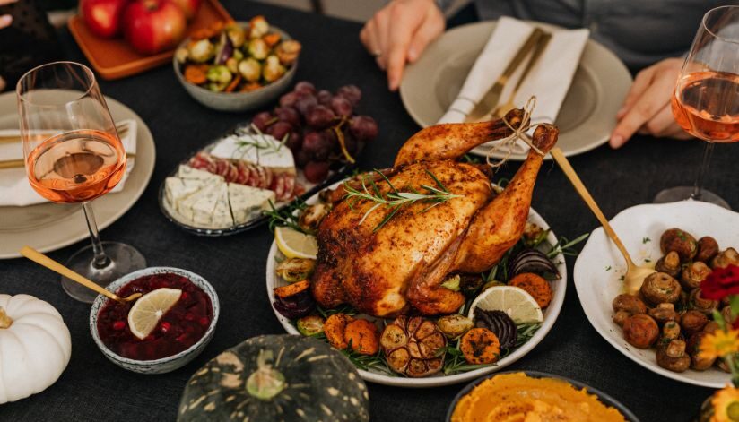 Holiday party guests enjoy roast chicken, sides, and wine at a festive table.